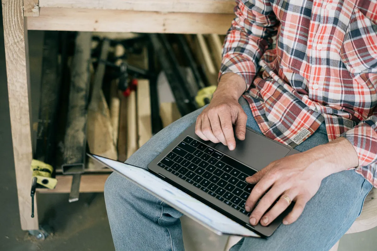 Τεχνίτης σε εργαστήριο δουλεύει σε laptop ανάμεσα σε εργαλεία